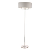 A heavy based metal floor lamp finished in reflective polished nickel, with a silver grey shallow drum shade, that surrounds the top bulb holder which frame is partially visible peeking beneath the shade, the light has three bulbs on a frame with arms inside the shade so it makes it a very bright light if required.
